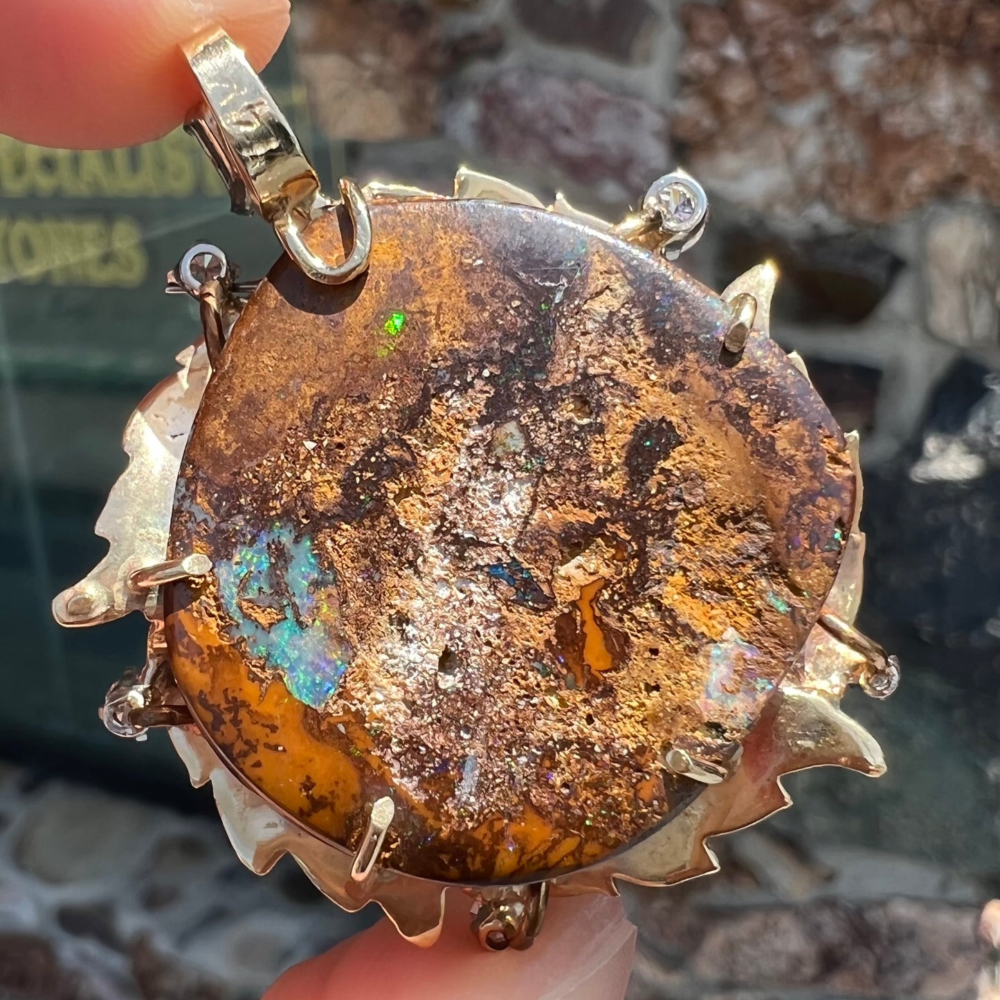 A gold opalized wood, diamond, and emerald pendant. The opal is set in a wreath of gold feathers that form a star.