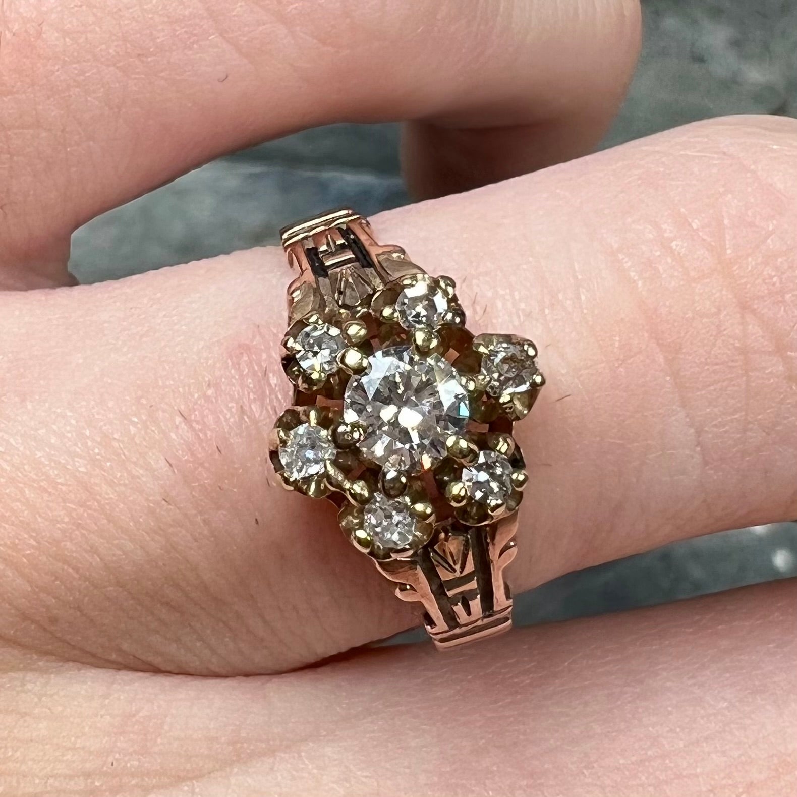 A modern Standard Round Brilliant Cut diamond set between six smaller round diamonds in an antique rose gold engagement ring setting.