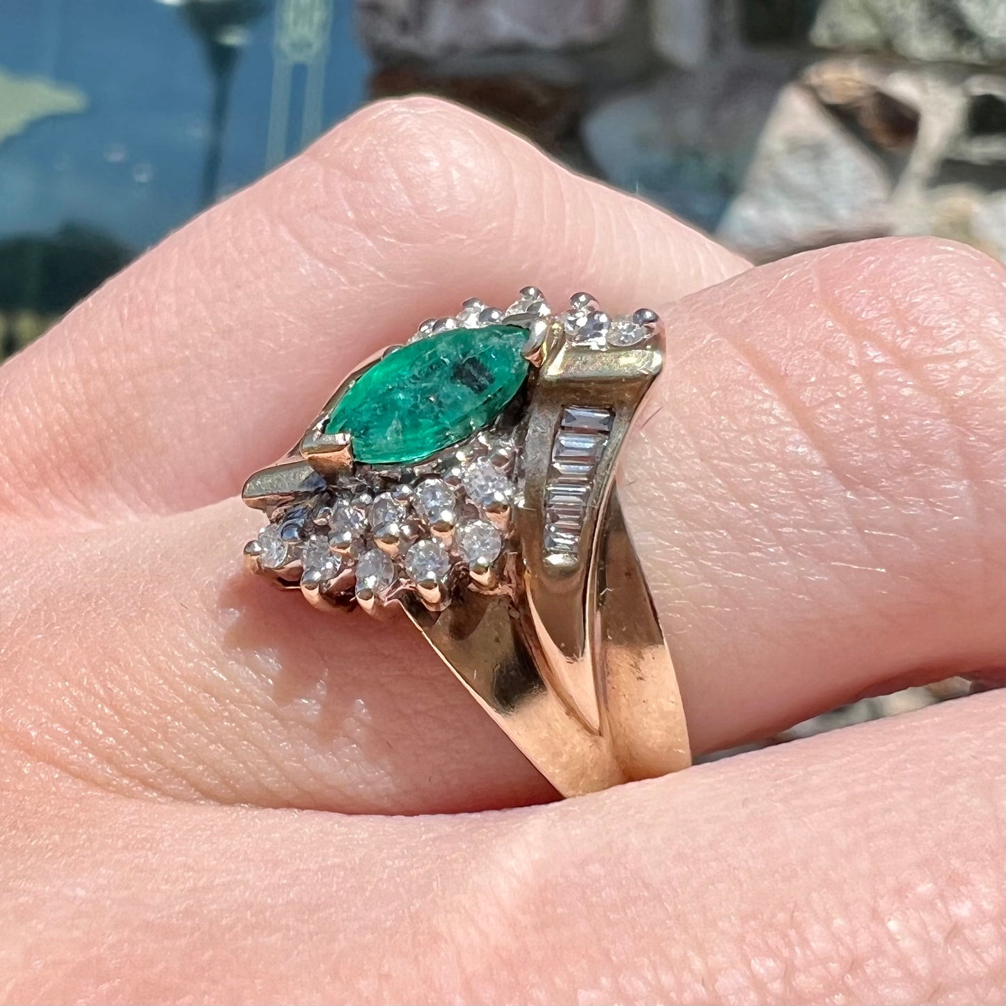 A yellow gold marquise cut emerald and diamond ring. The diamonds are prong set round cuts and channel set baguette cuts.
