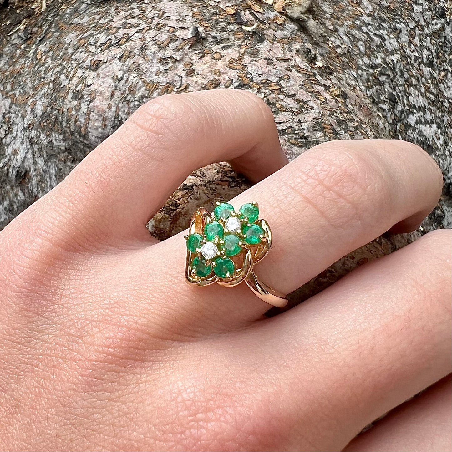 A yellow gold ring set with round cut emerald and diamonds that form the shape of two flowers.