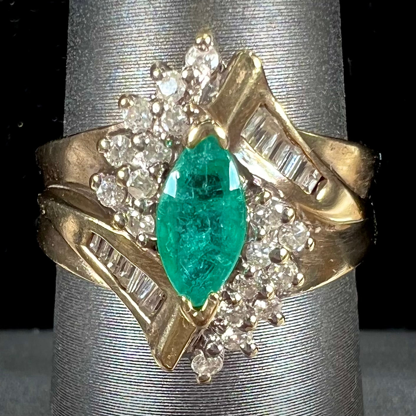 A yellow gold marquise cut emerald and diamond ring. The diamonds are prong set round cuts and channel set baguette cuts.