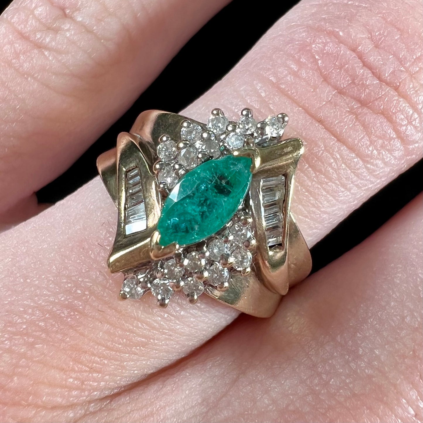 A yellow gold marquise cut emerald and diamond ring. The diamonds are prong set round cuts and channel set baguette cuts.