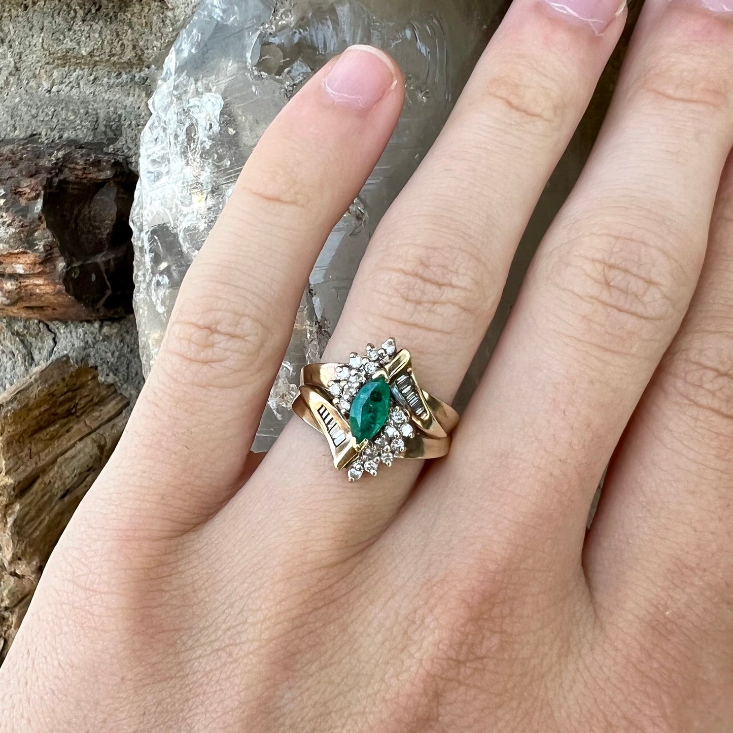 A yellow gold marquise cut emerald and diamond ring. The diamonds are prong set round cuts and channel set baguette cuts.