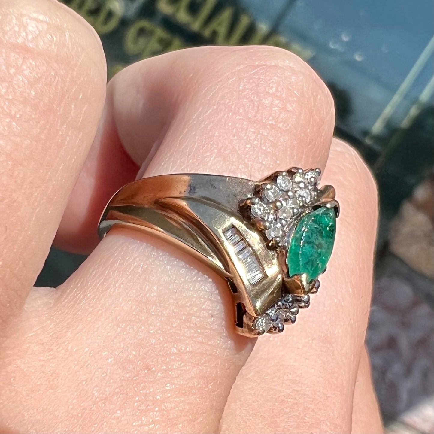 A yellow gold marquise cut emerald and diamond ring. The diamonds are prong set round cuts and channel set baguette cuts.