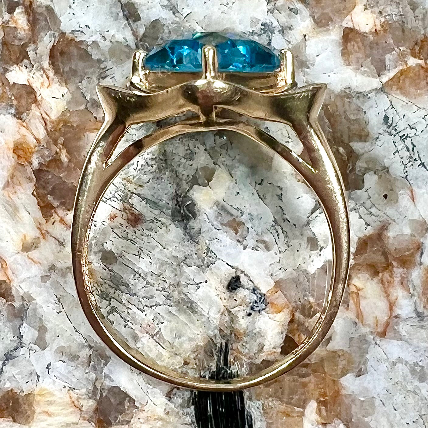 A checkerboard princess cut Swiss blue topaz ring. The stone is set in a yellow gold, diamond halo mounting.