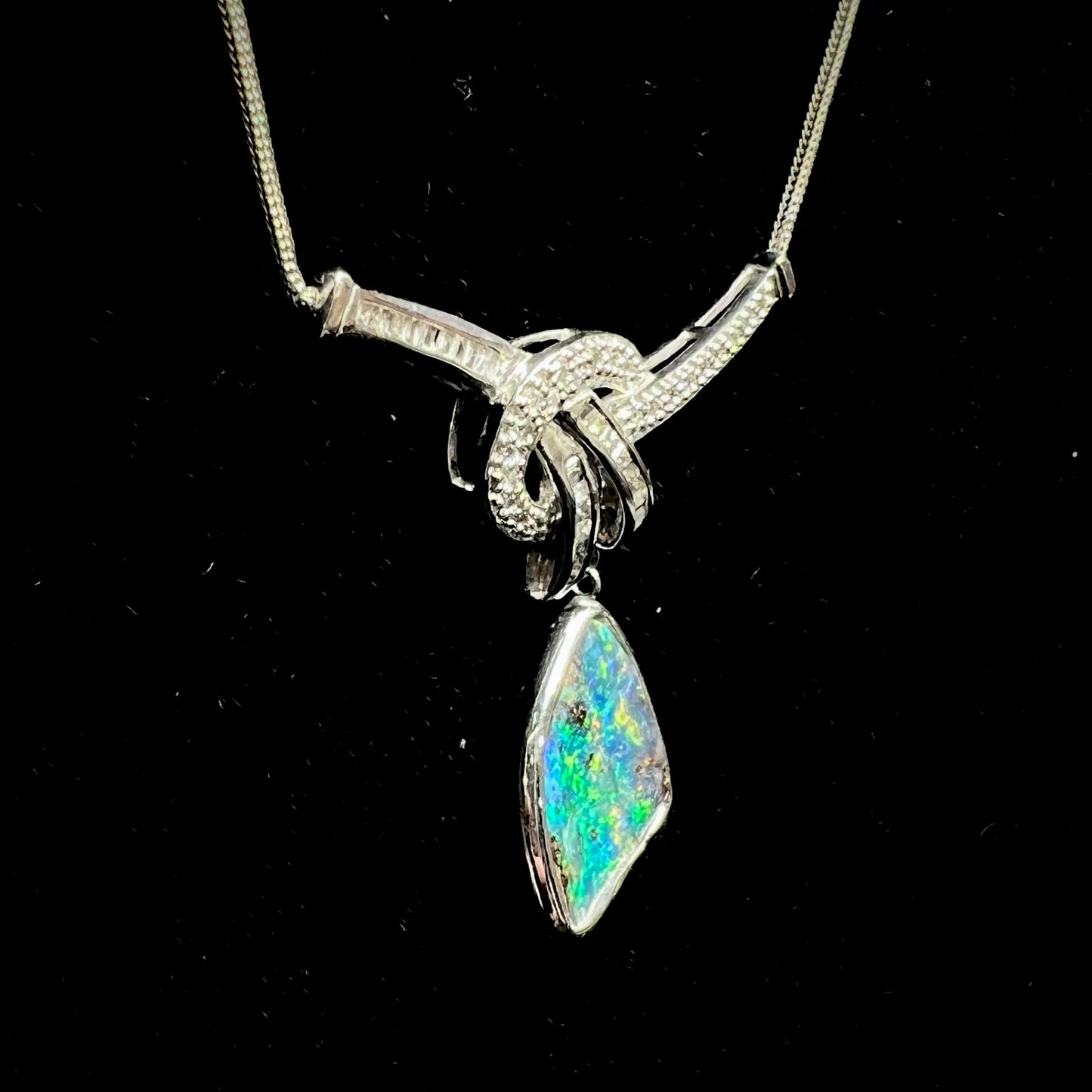 A white gold necklace set with diamonds and a dangling, bezel set boulder opal.