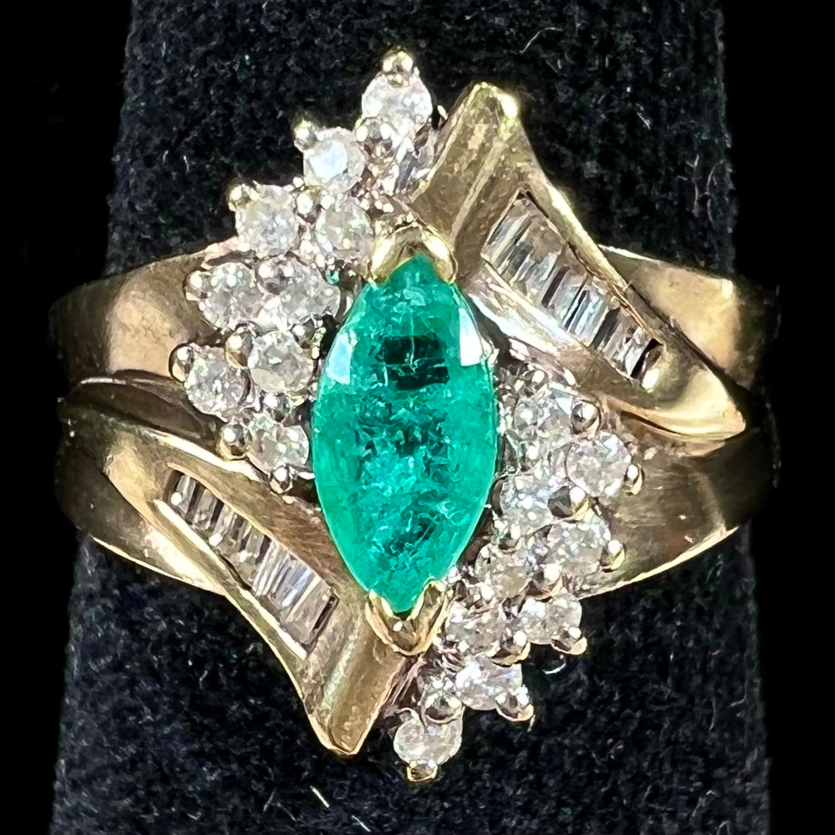 A yellow gold marquise cut emerald and diamond ring. The diamonds are prong set round cuts and channel set baguette cuts.