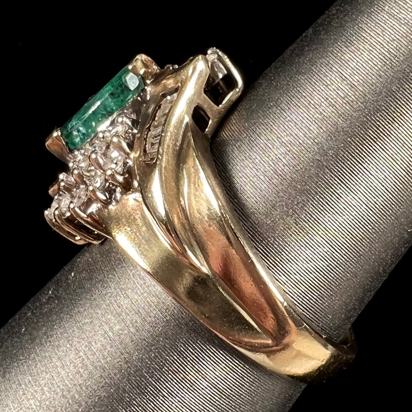 A yellow gold marquise cut emerald and diamond ring. The diamonds are prong set round cuts and channel set baguette cuts.