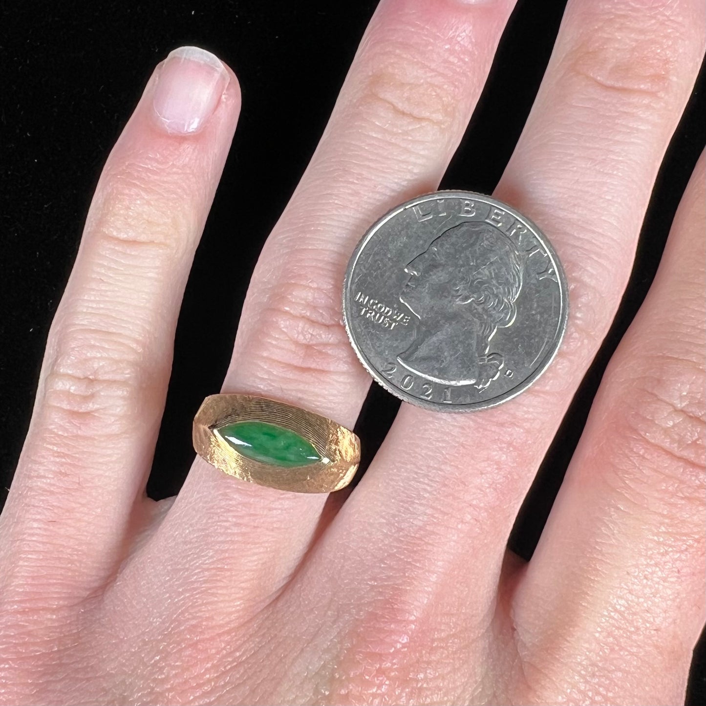 A textured yellow gold ring set with a marquise cabochon cut green jadeite stone.