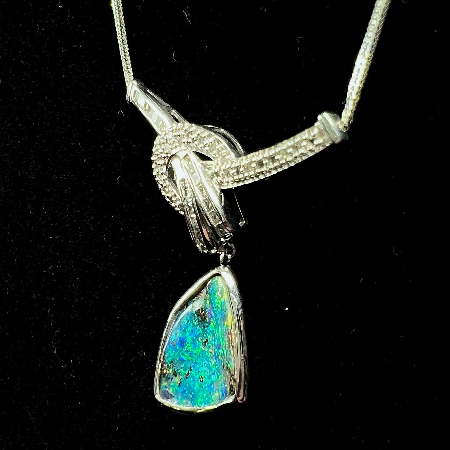 A white gold necklace set with diamonds and a dangling, bezel set boulder opal.