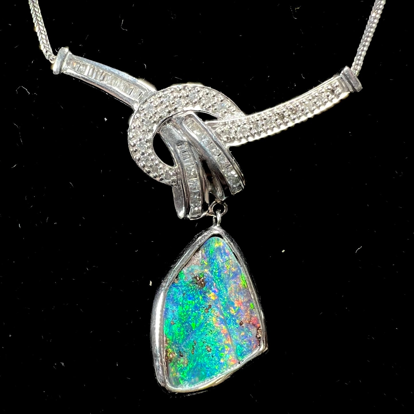 A white gold necklace set with diamonds and a dangling, bezel set boulder opal.