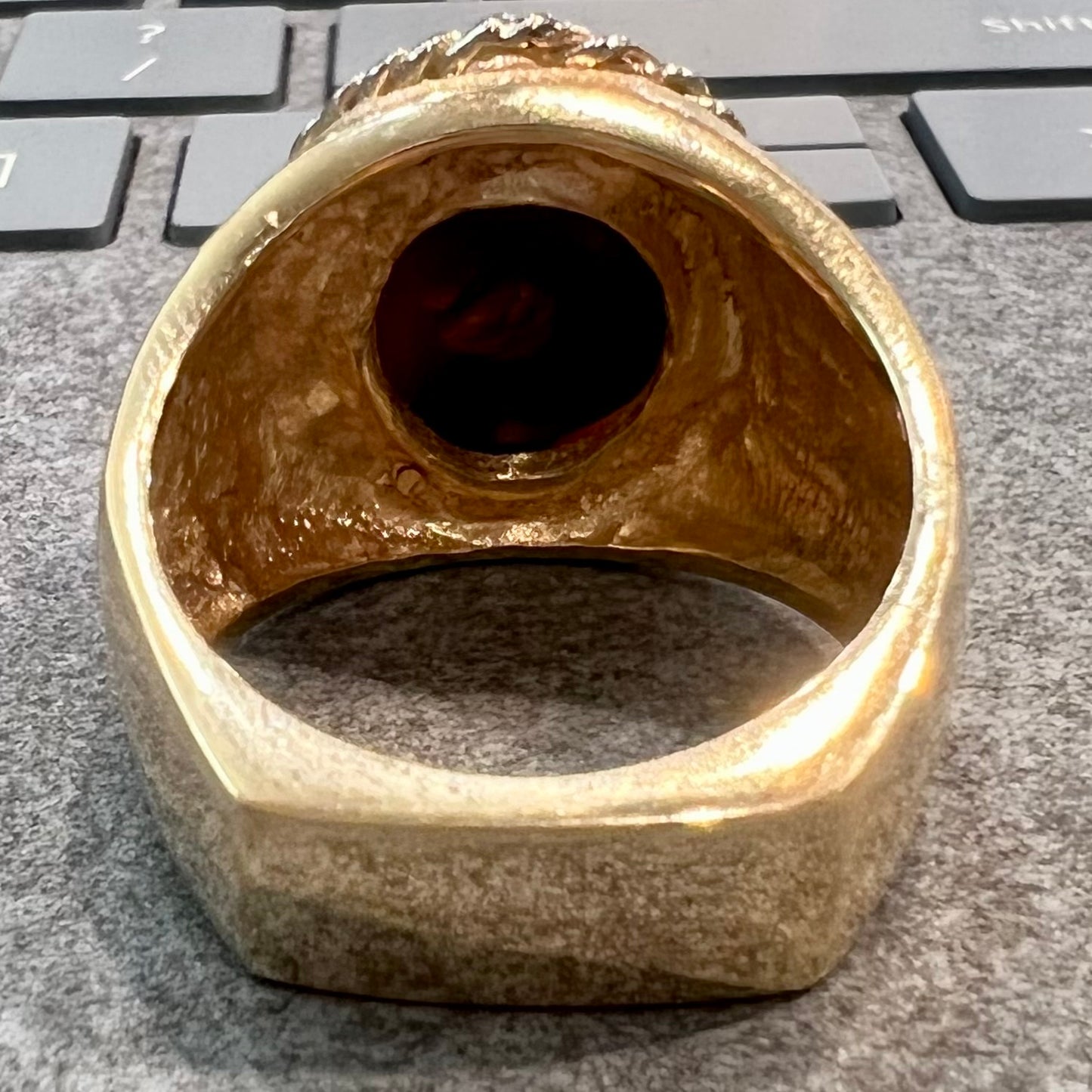 A men's matte finish textured gold fire agate ring. There is a gold rope bezel around the oval cabochon cut stone.