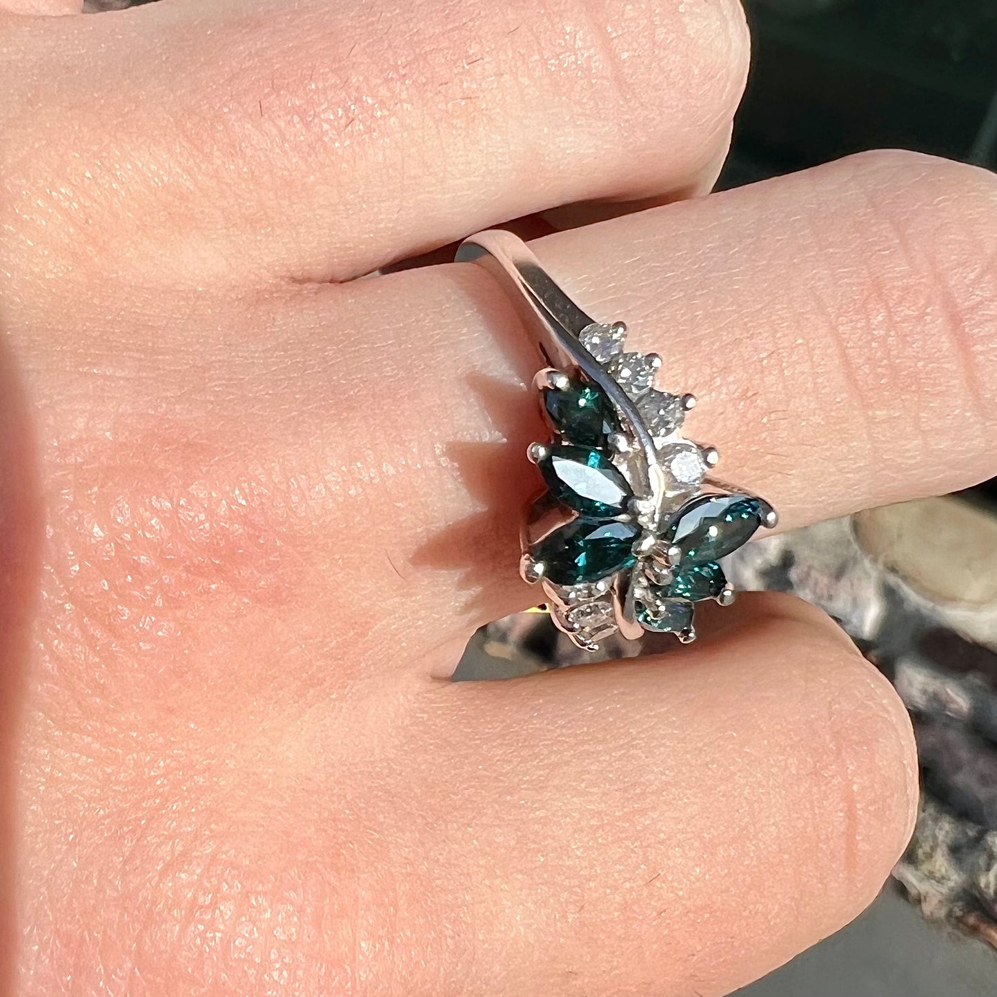 A white gold diamond cluster ring set with blue marquise cut and white round cut diamonds.