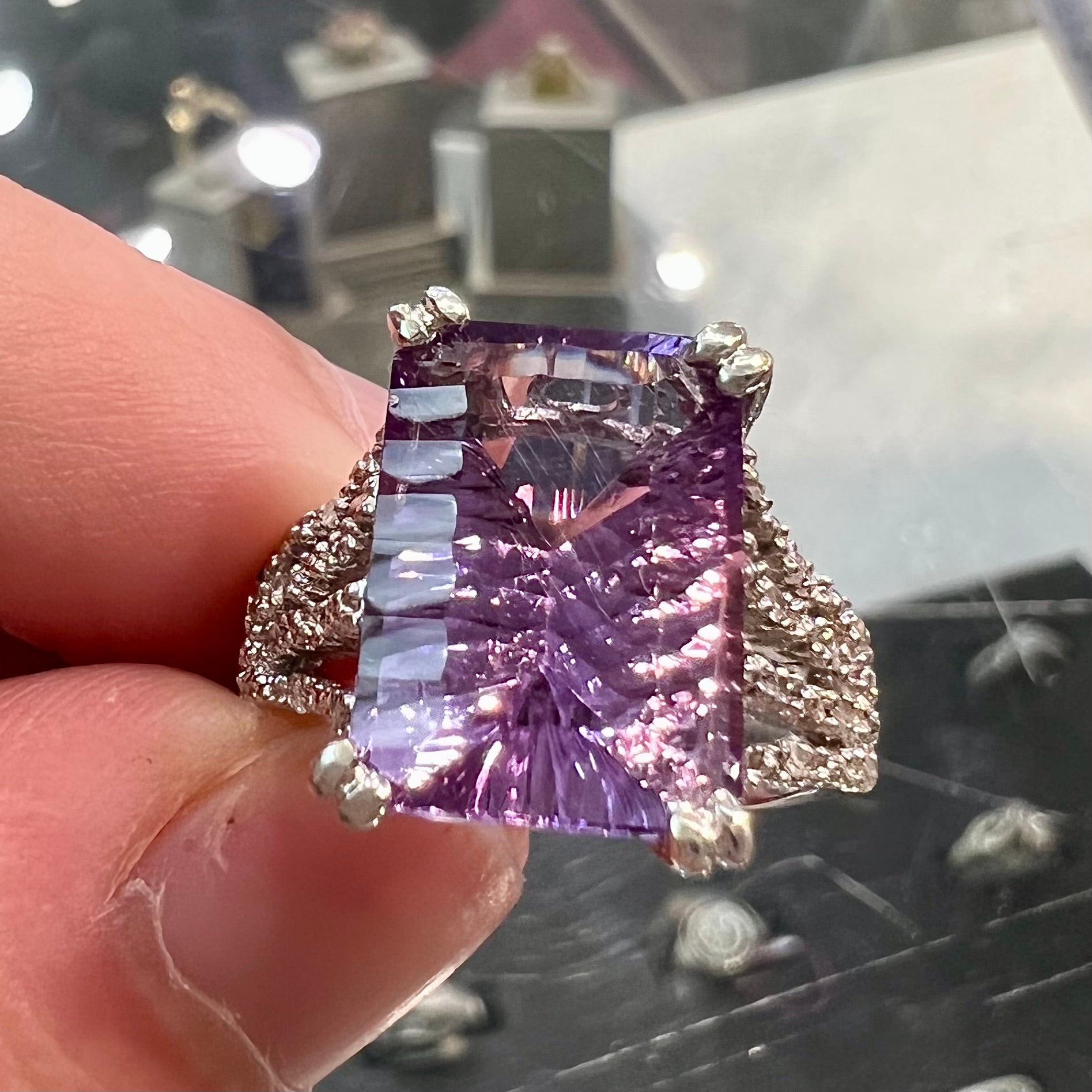 A white gold ladies ring set with an emerald laser cut amethyst and diamond chip accents.