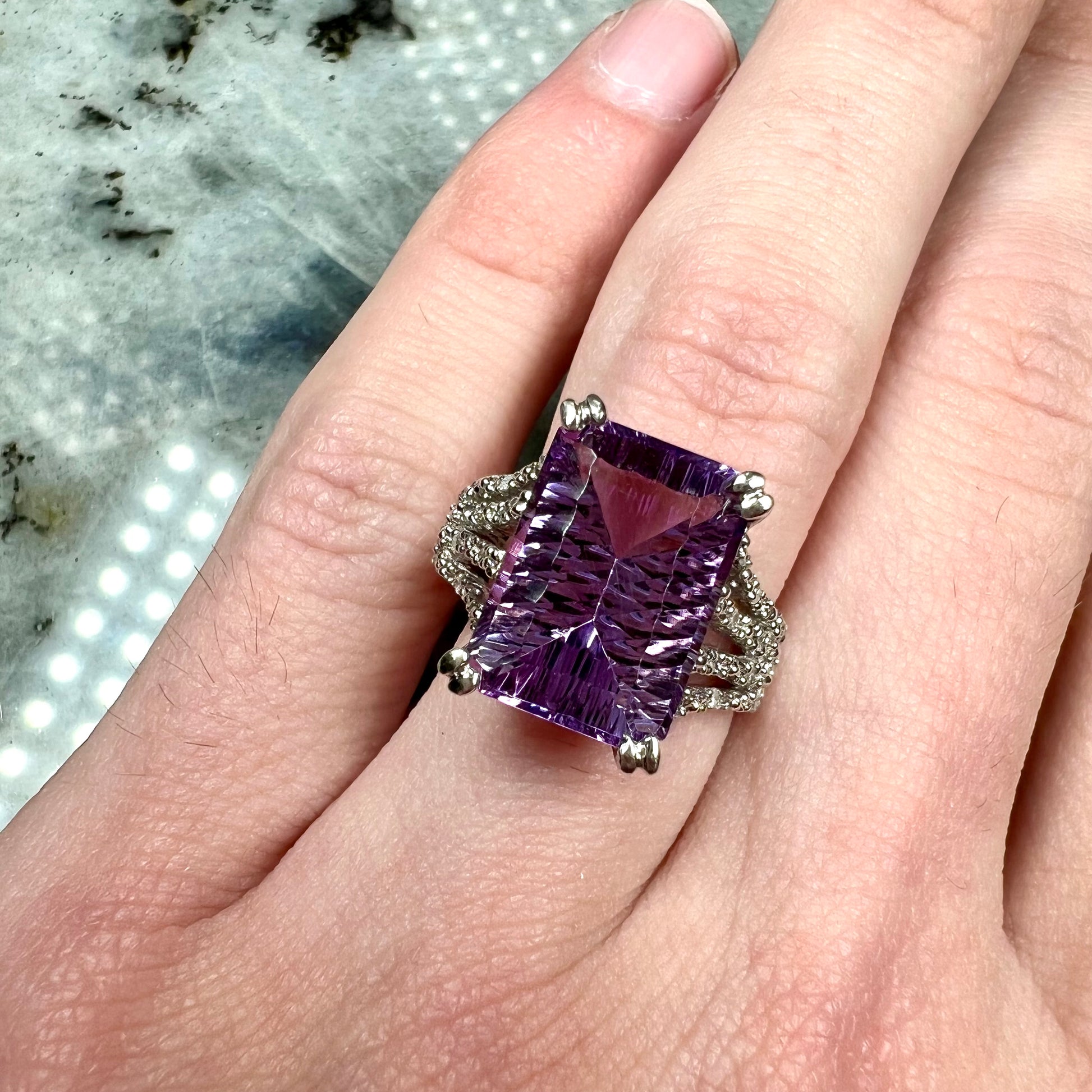 A white gold ladies ring set with an emerald laser cut amethyst and diamond chip accents.