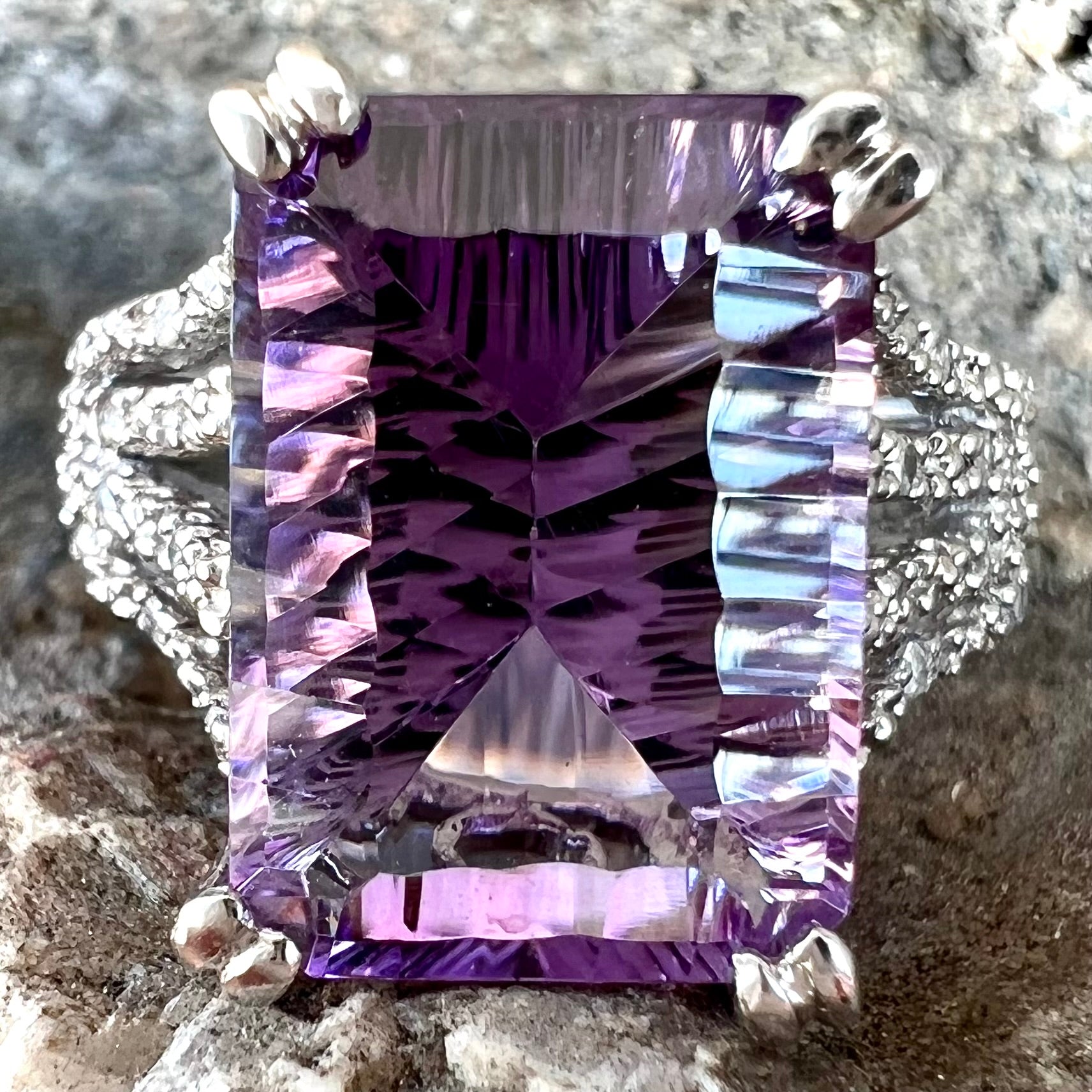 A white gold ladies ring set with an emerald laser cut amethyst and diamond chip accents.