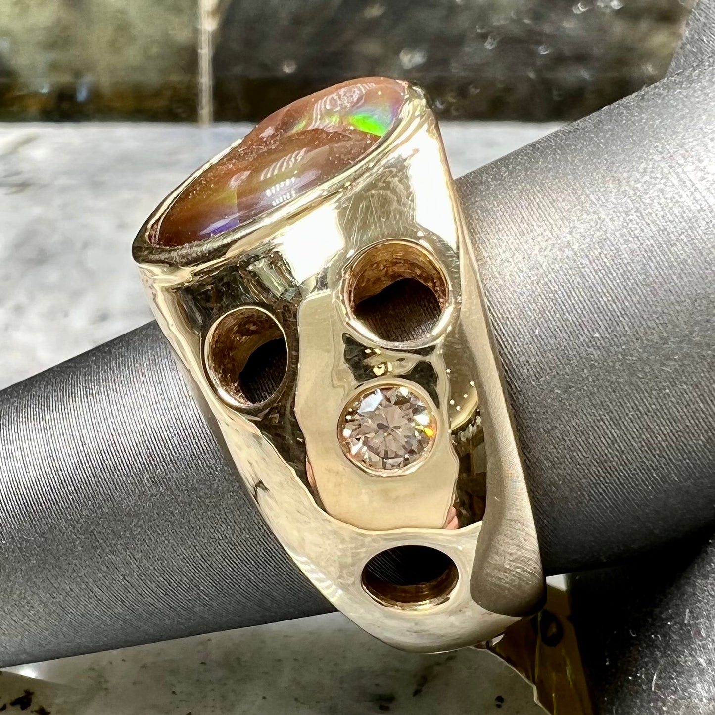 Men's rainbow fire agate ring set in yellow gold with champagne diamonds. The ring style has holes.