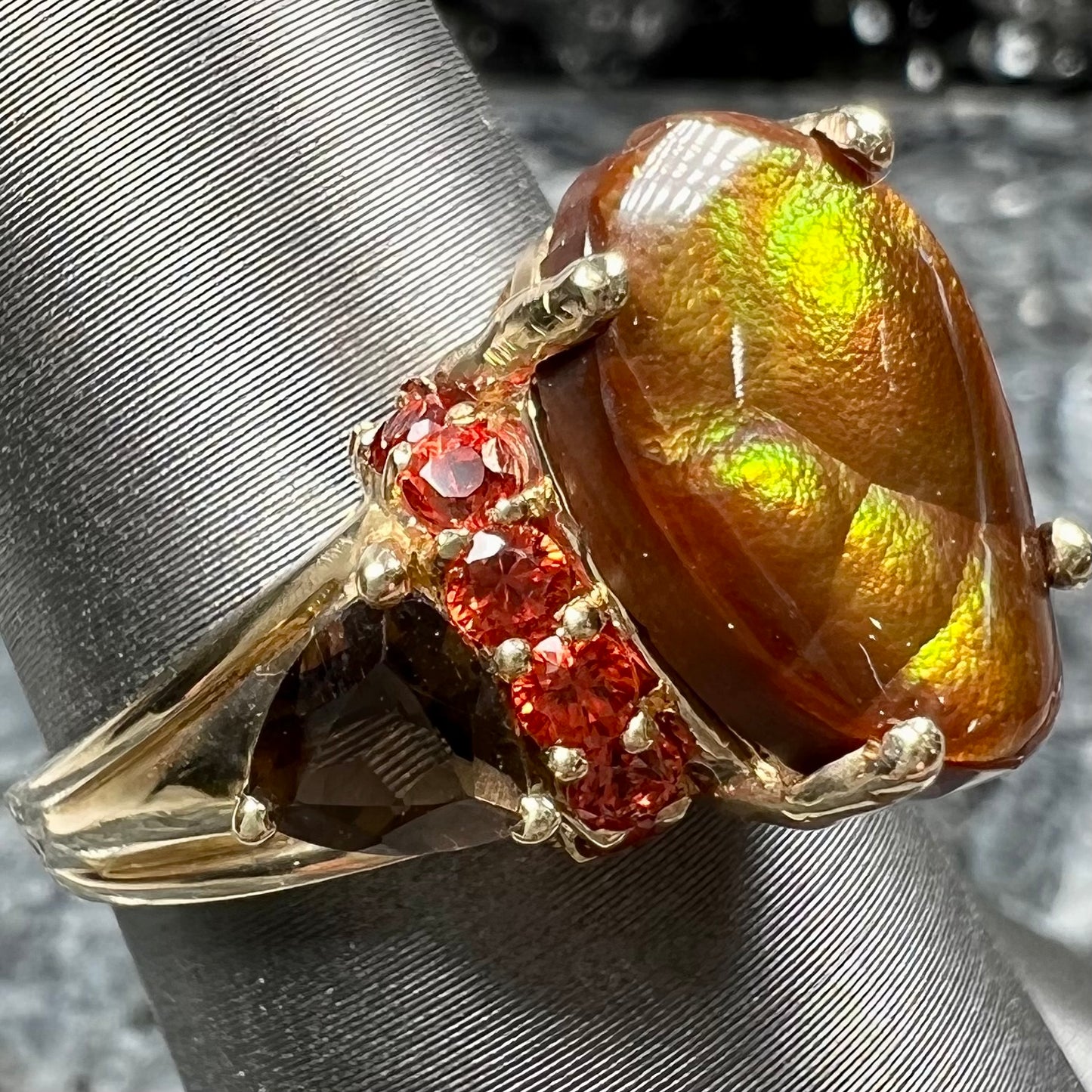 A ladies yellow gold fire agate ring set with trillion cut smoky quartz and round cut red-orange garnet accents. The fire agate displays green and red.