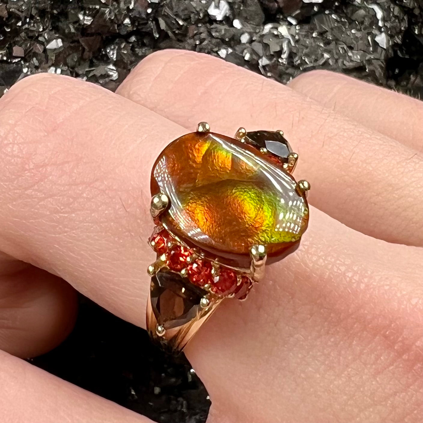 A ladies yellow gold fire agate ring set with trillion cut smoky quartz and round cut red-orange garnet accents. The fire agate displays green and red.