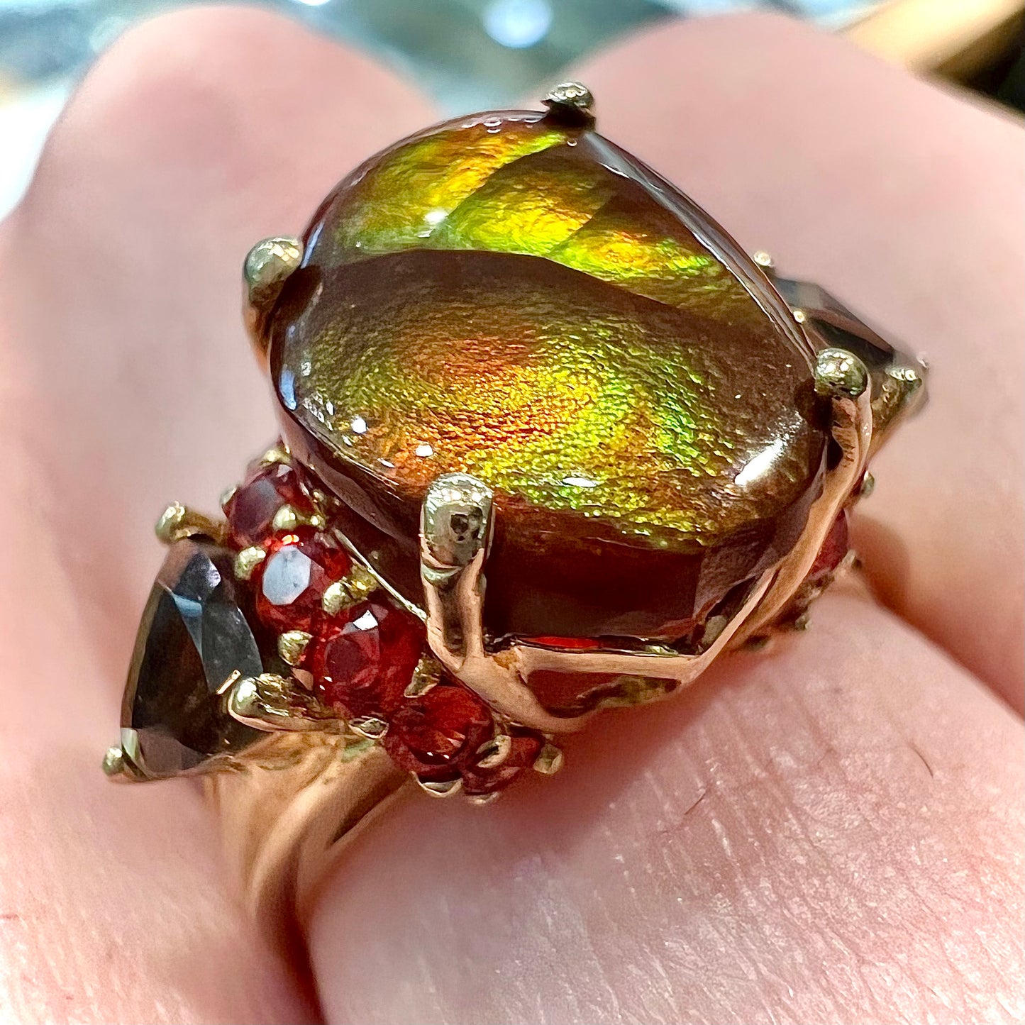 A ladies yellow gold fire agate ring set with trillion cut smoky quartz and round cut red-orange garnet accents. The fire agate displays green and red.