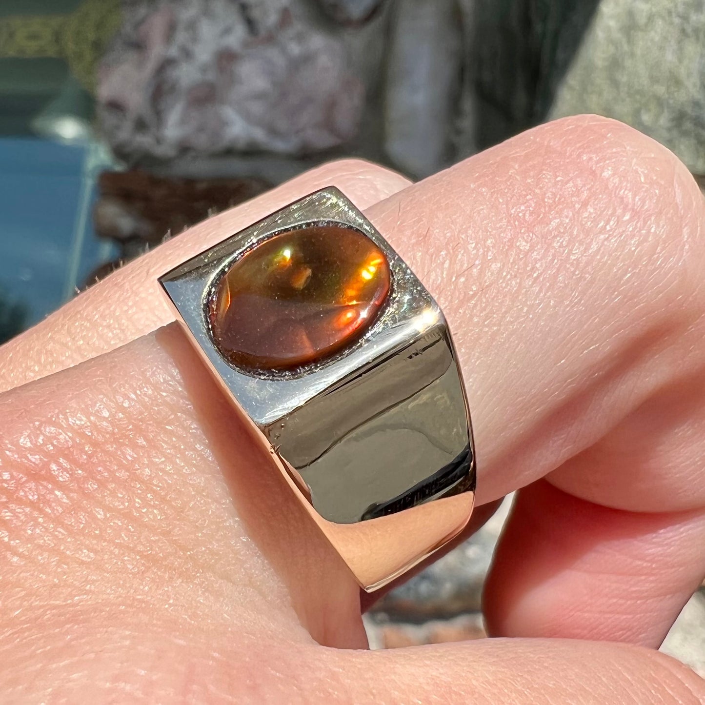 A men's yellow gold flush set fire agate solitaire ring. The fire agate displays flashes of green, orange, and yellow.