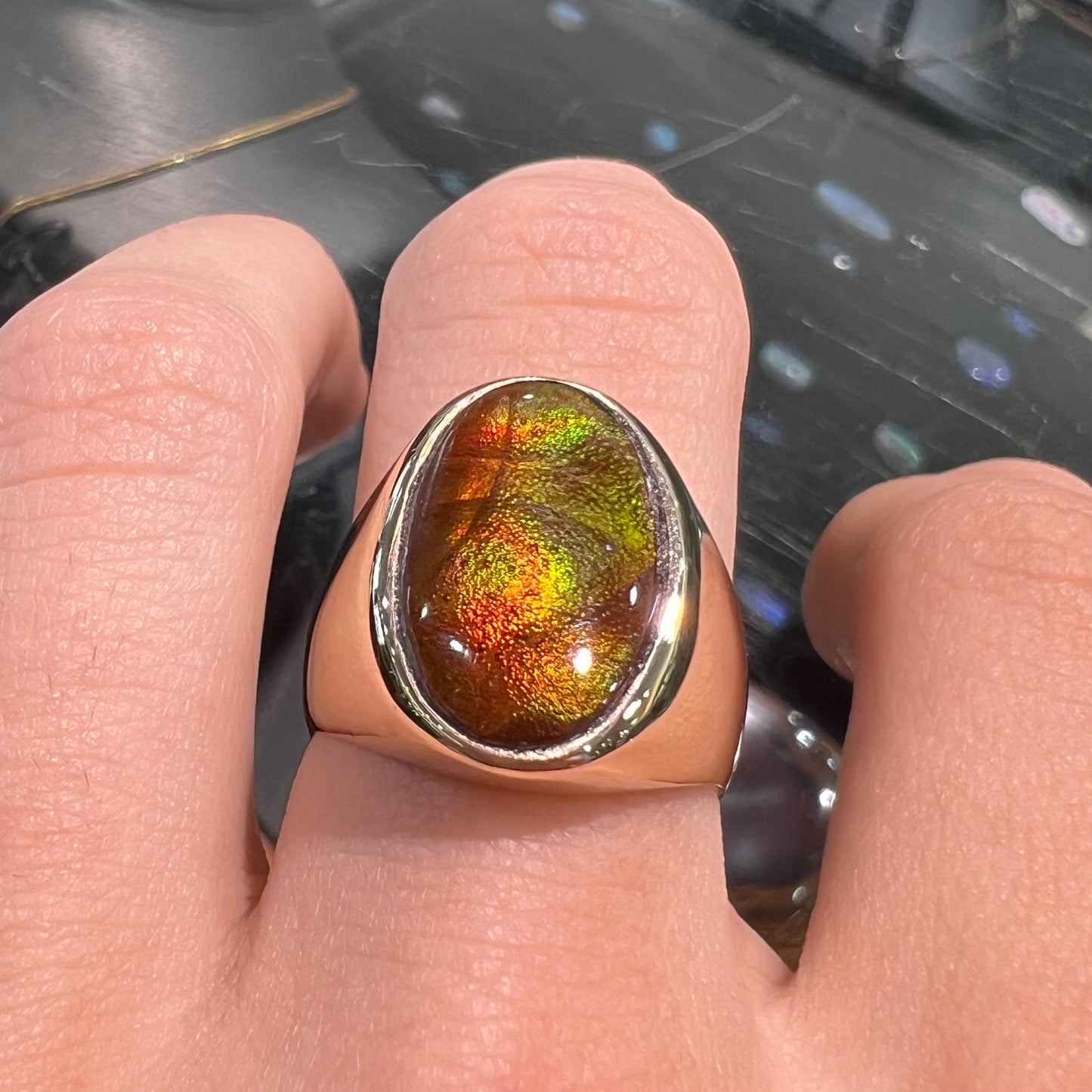 A yellow gold solitaire fire agate men's ring. The fire agate is oval shape, and red and green in color.