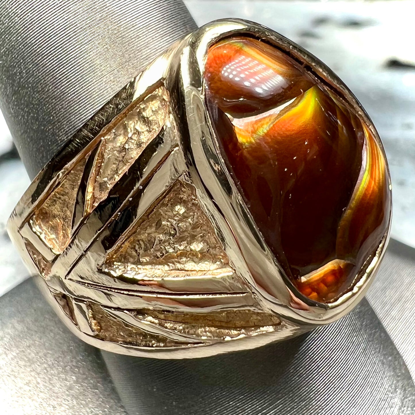 A solid, yellow gold men's fire agate ring. The predominant color is red with green undertones.