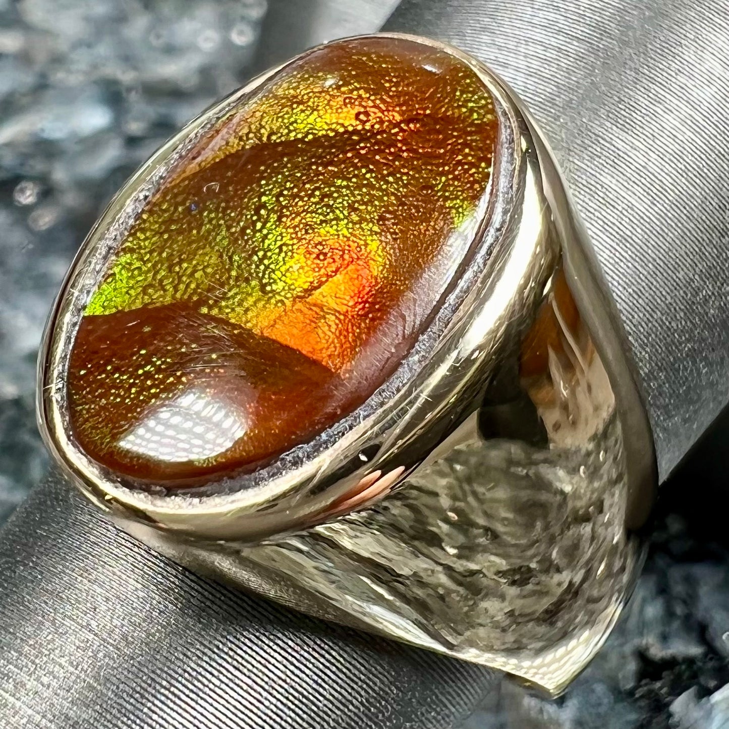 A yellow gold solitaire fire agate men's ring. The fire agate is oval shape, and red and green in color.