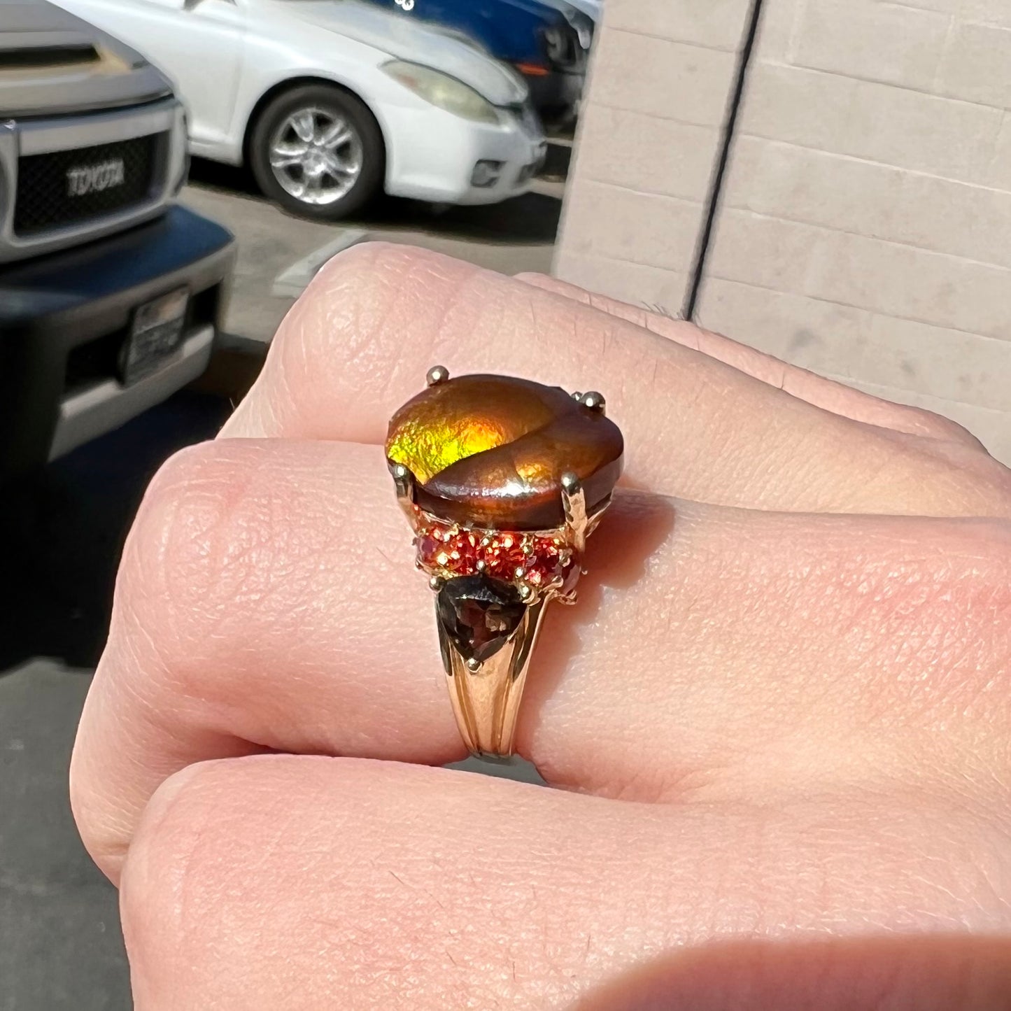 A ladies yellow gold fire agate ring set with trillion cut smoky quartz and round cut red-orange garnet accents. The fire agate displays green and red.