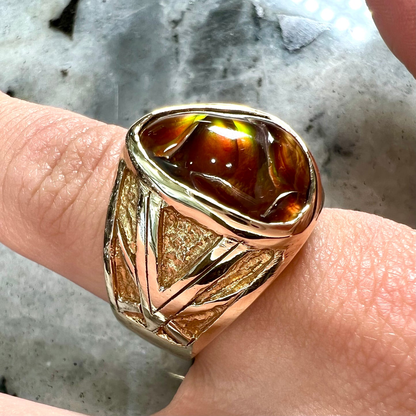 A solid, yellow gold men's fire agate ring. The predominant color is red with green undertones.