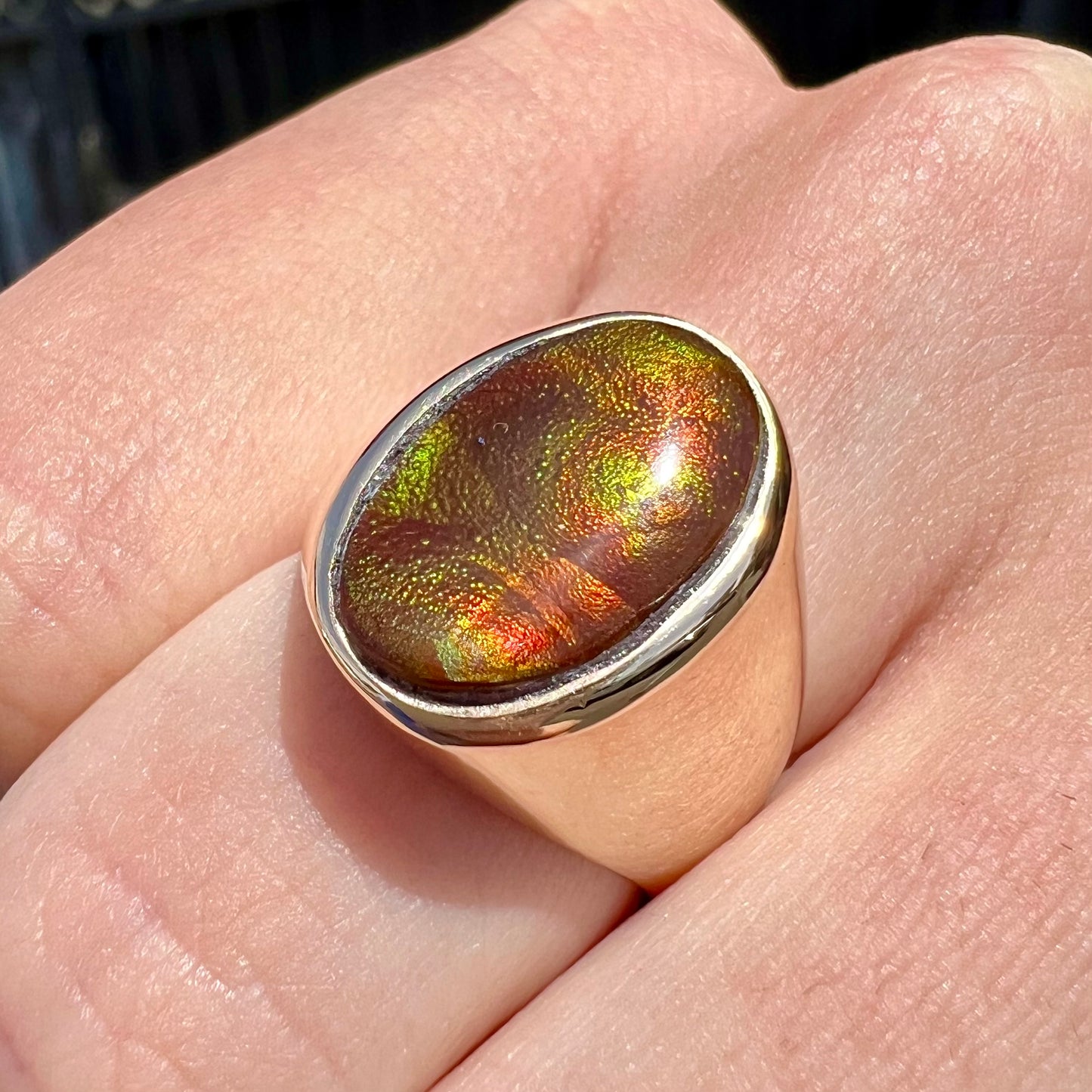 A yellow gold solitaire fire agate men's ring. The fire agate is oval shape, and red and green in color.