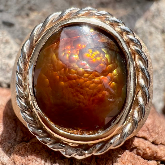 A men's matte finish textured gold fire agate ring.  There is a gold rope bezel around the oval cabochon cut stone.