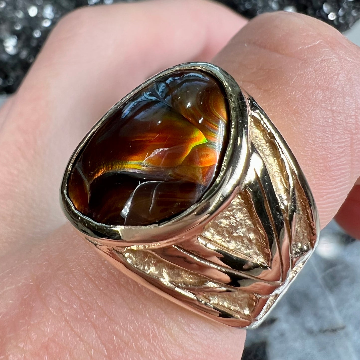 A solid, yellow gold men's fire agate ring. The predominant color is red with green undertones.