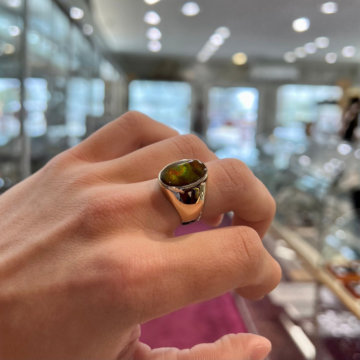 A yellow gold solitaire fire agate men's ring. The fire agate is oval shape, and red and green in color.