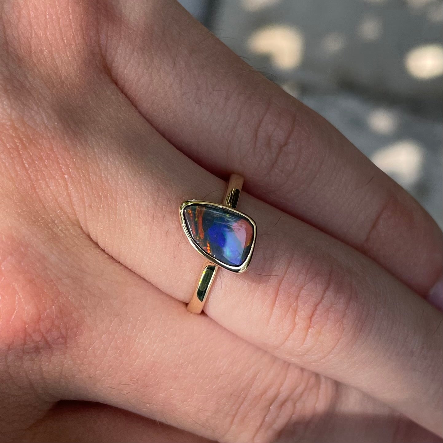 A handmade yellow gold solitaire ring bezel set with a Lightning Ridge red-on-black harlequin opal.