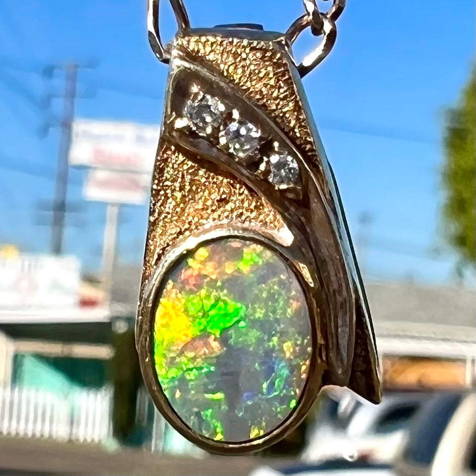 A yellow gold black opal necklace set with three round diamond accents.