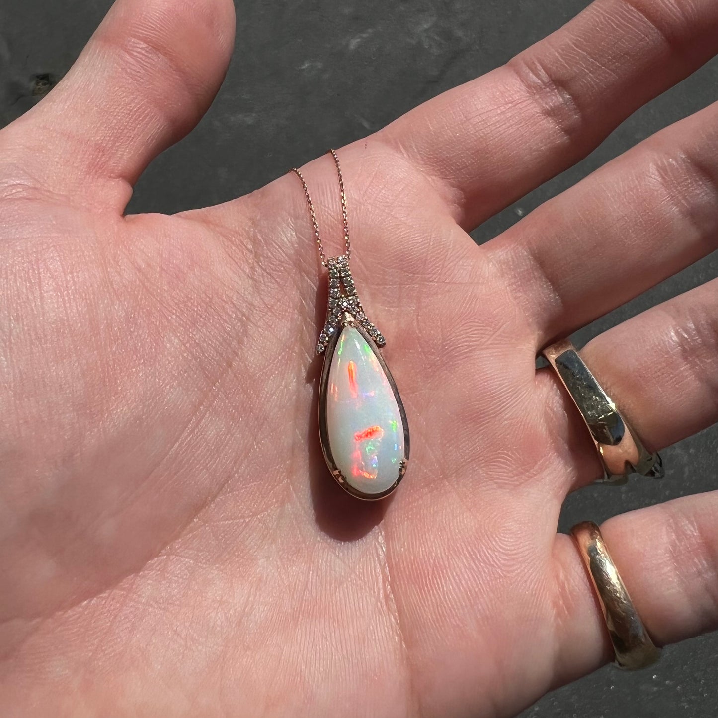 A rose gold, teardrop shaped fire opal and diamond necklace on a cable chain.
