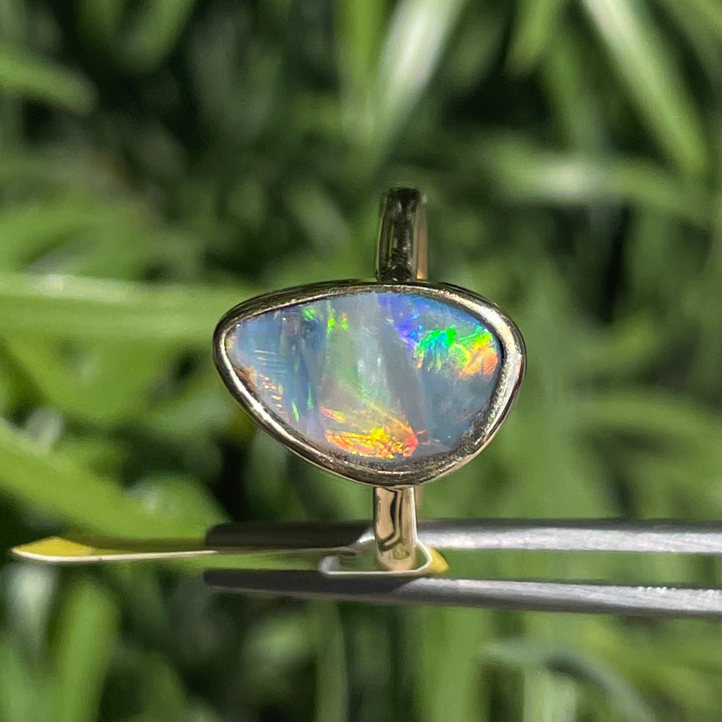 A freeform cut semi-black opal from Lightning Ridge, Australia set in a bezel set yellow gold solitaire ring.