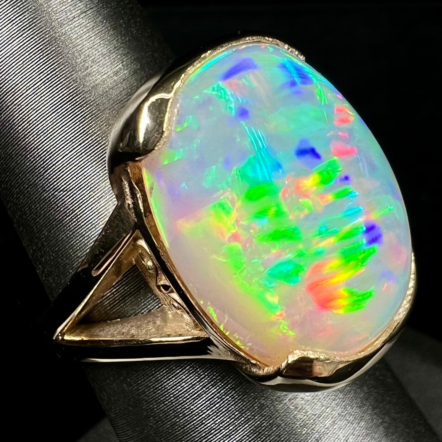 A ladies' yellow gold split shank ring half-bezel set with a barrel cabochon cut natural Ethiopian fire opal stone.