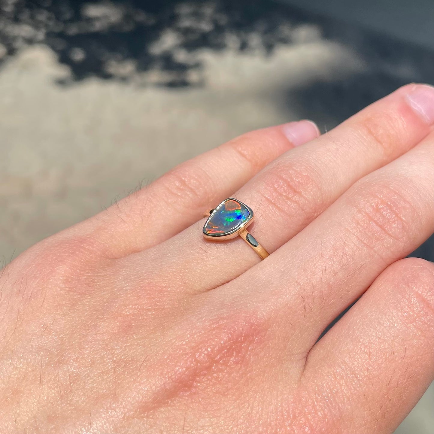 A handmade yellow gold solitaire ring bezel set with a Lightning Ridge red-on-black harlequin opal.