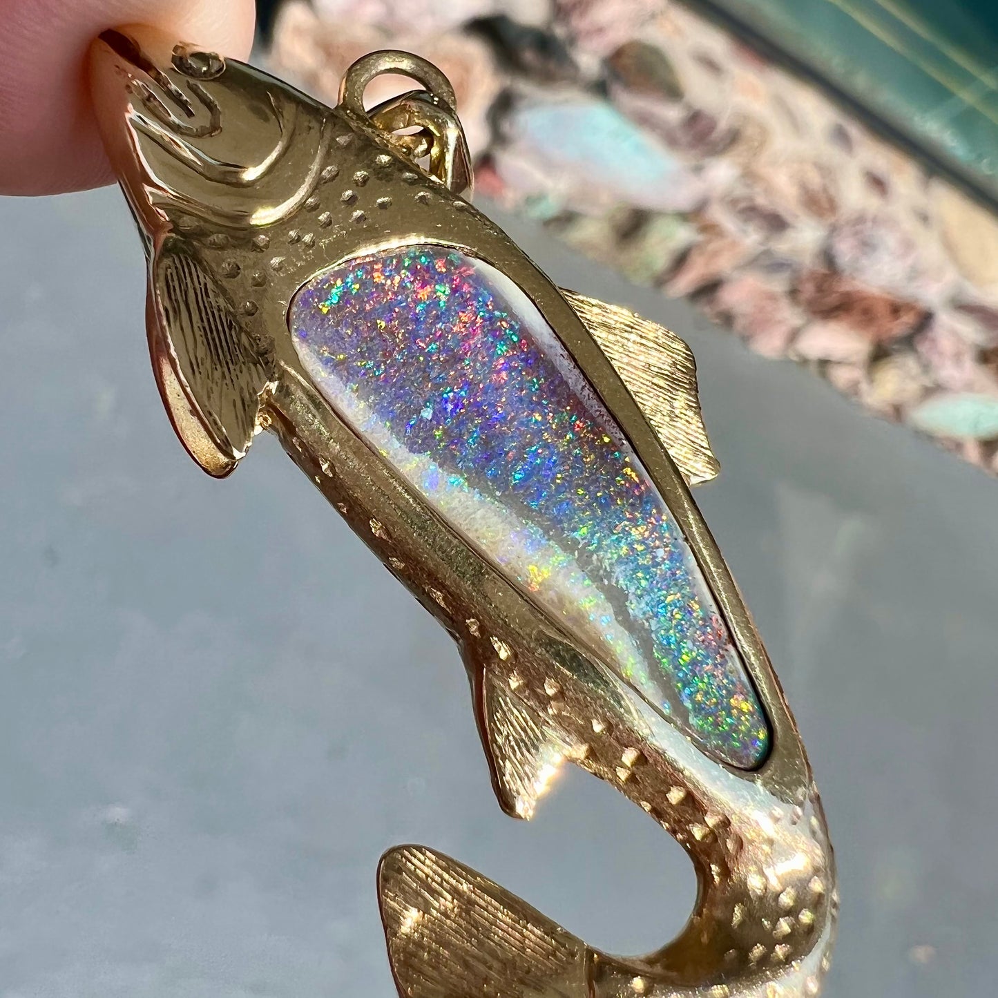 A yellow gold fish pendant detailed to look like a rainbow trout. The body of the fish is set with a color changing black opal stone.