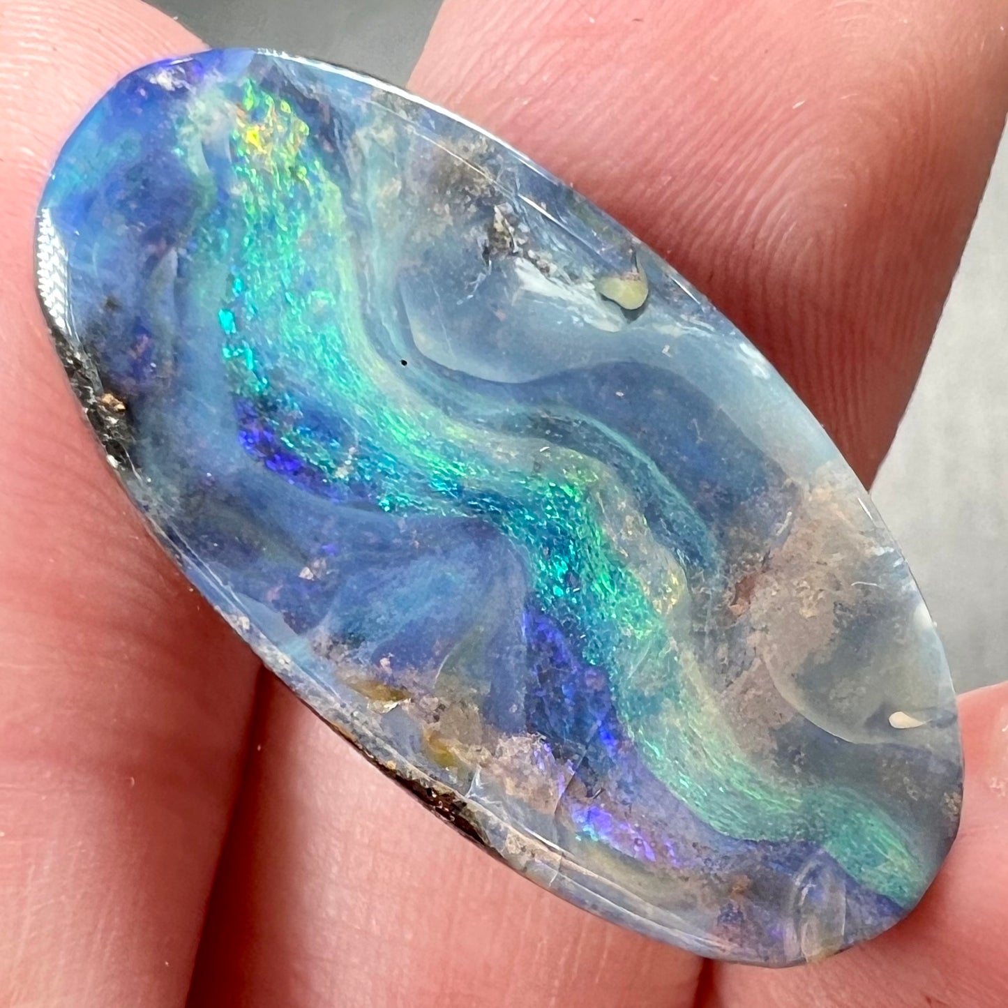 A loose, oval cabochon cut Quilpie boulder opal from Queensland, Australia. The stone is blue with green fire.