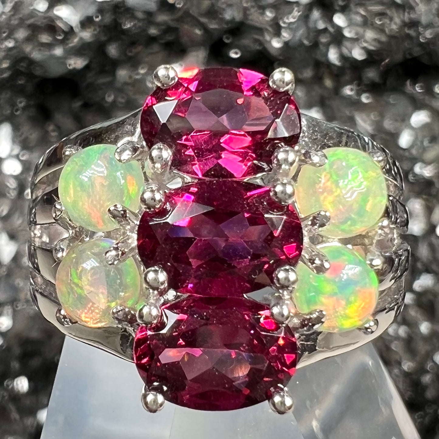 A sterling silver ring set with three oval cut rhodolite garnets and four round cabochon cut Ethiopian opals.