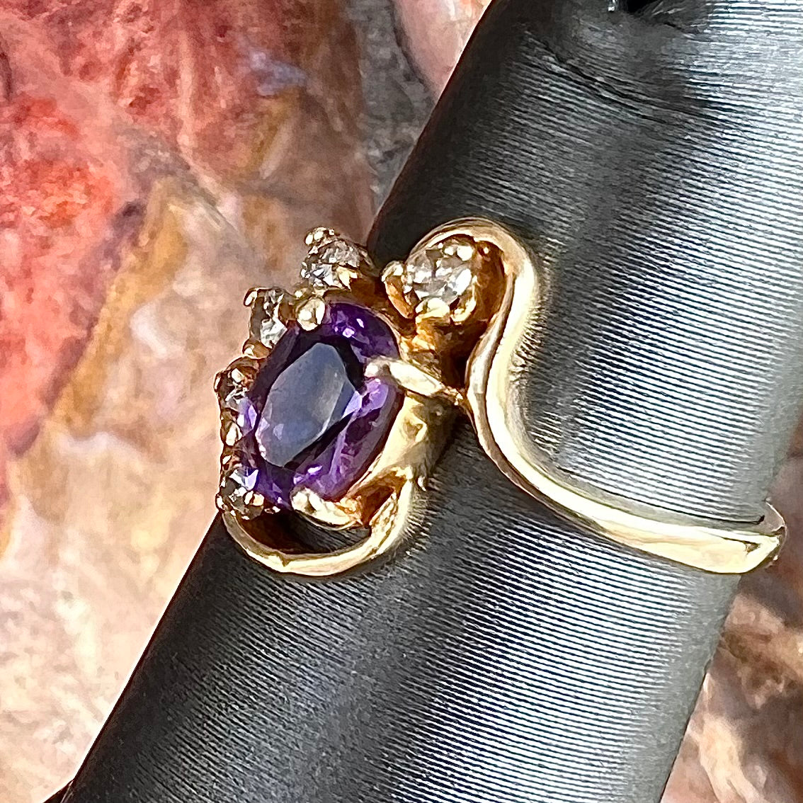 A ring made with 14 karat yellow gold, diamonds, and an amethyst. The ring has a swoosh style.