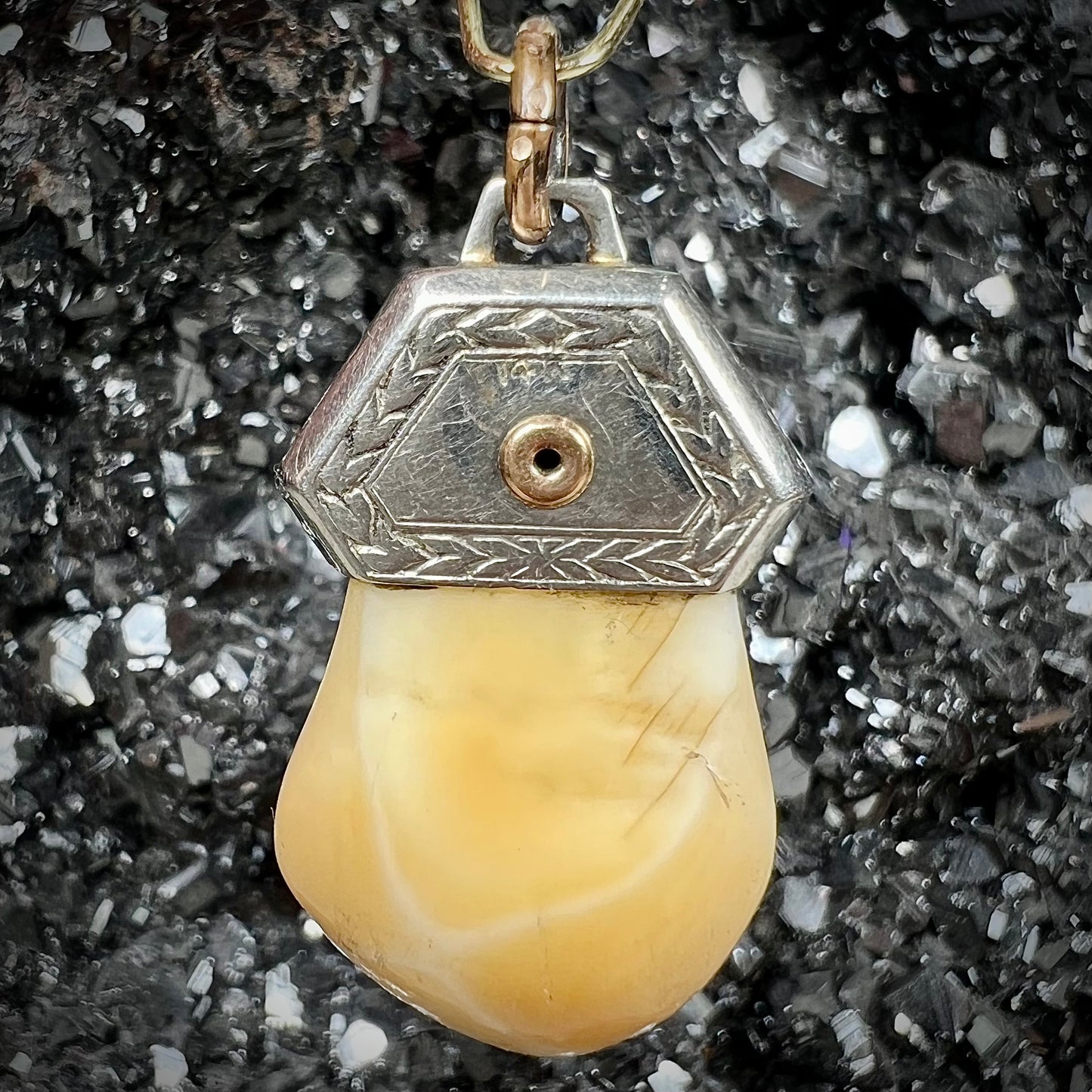 An elk tooth that has been fashioned into a blue enameled gold pendant. There is a decorative elk head cast in yellow gold set on the piece.