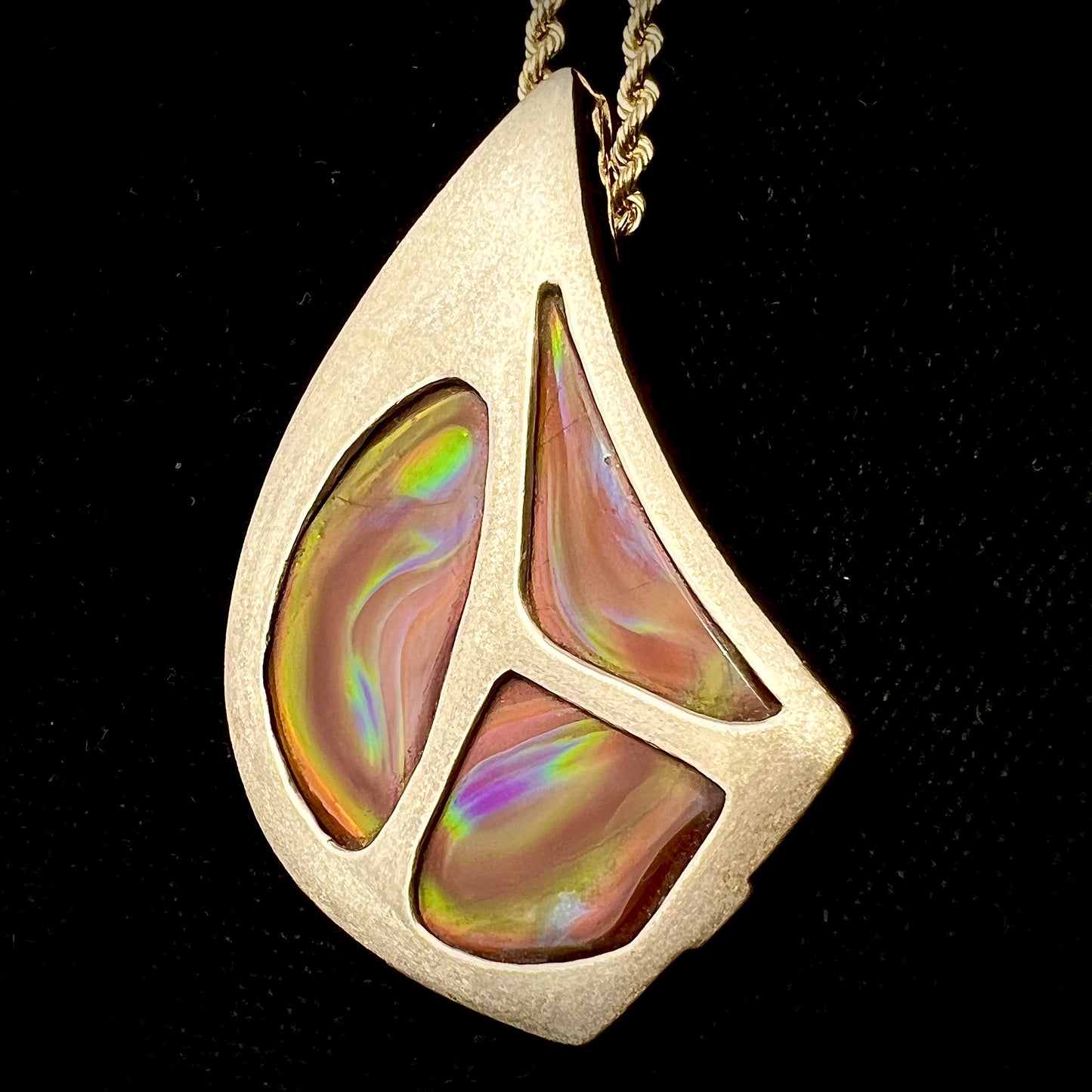A men's gold pendant set with three fire agate stones. The fire agate resembles an oil slick puddle.