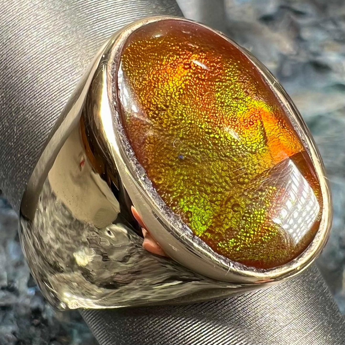 A yellow gold solitaire fire agate men's ring. The fire agate is oval shape, and red and green in color.