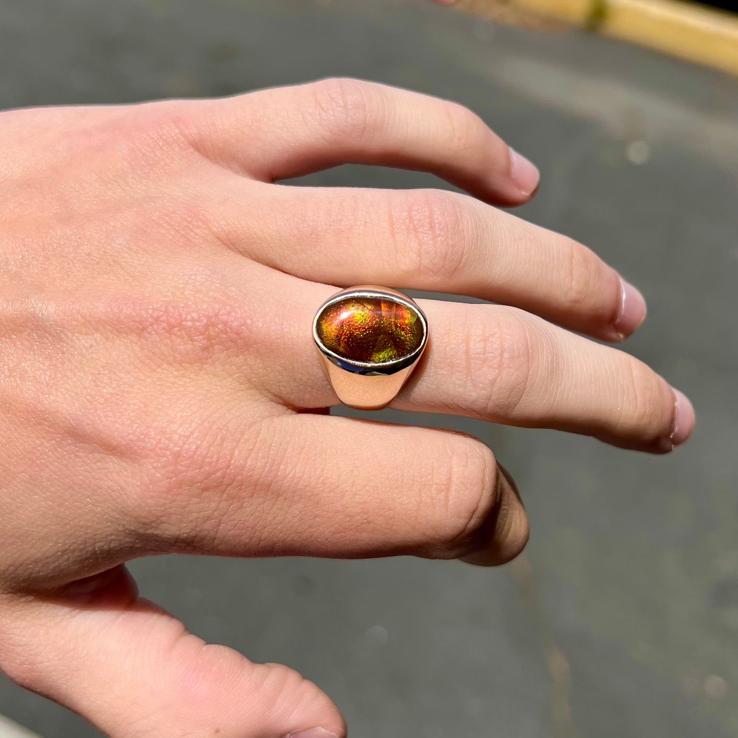 A yellow gold solitaire fire agate men's ring. The fire agate is oval shape, and red and green in color.
