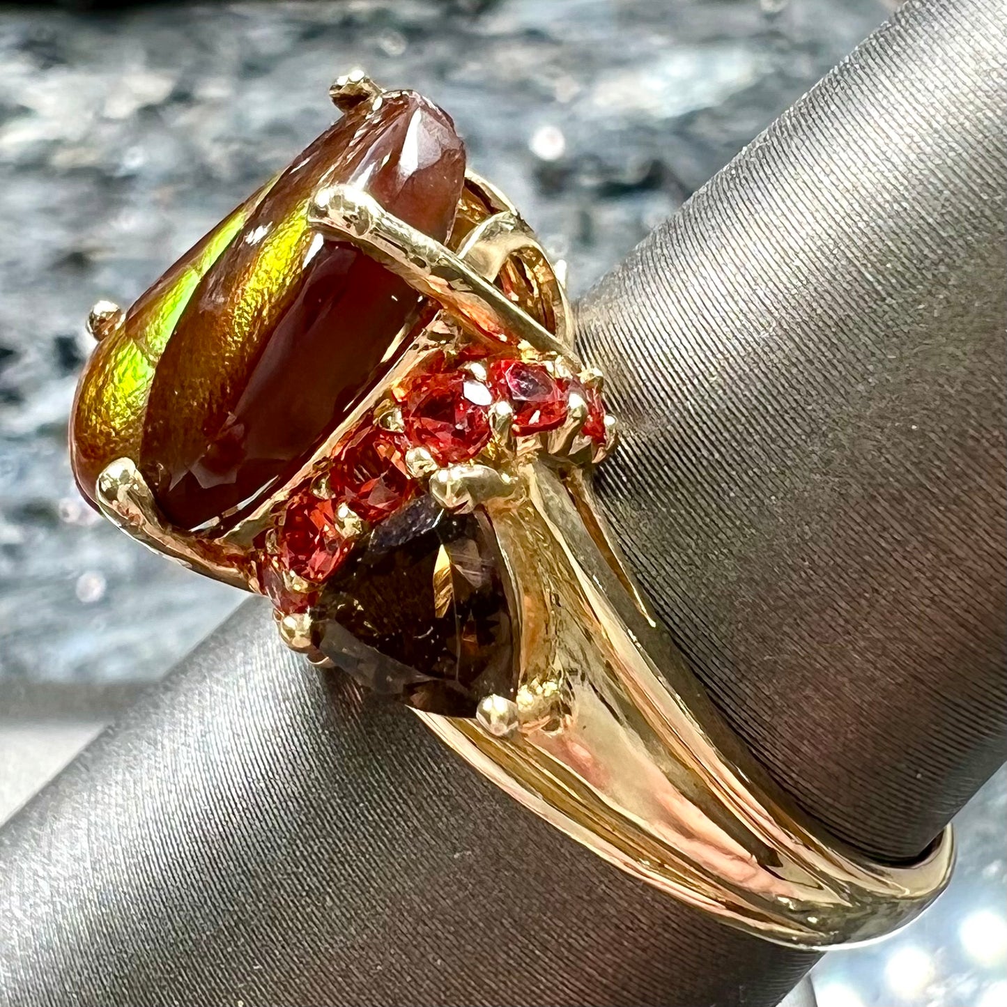 A ladies yellow gold fire agate ring set with trillion cut smoky quartz and round cut red-orange garnet accents. The fire agate displays green and red.