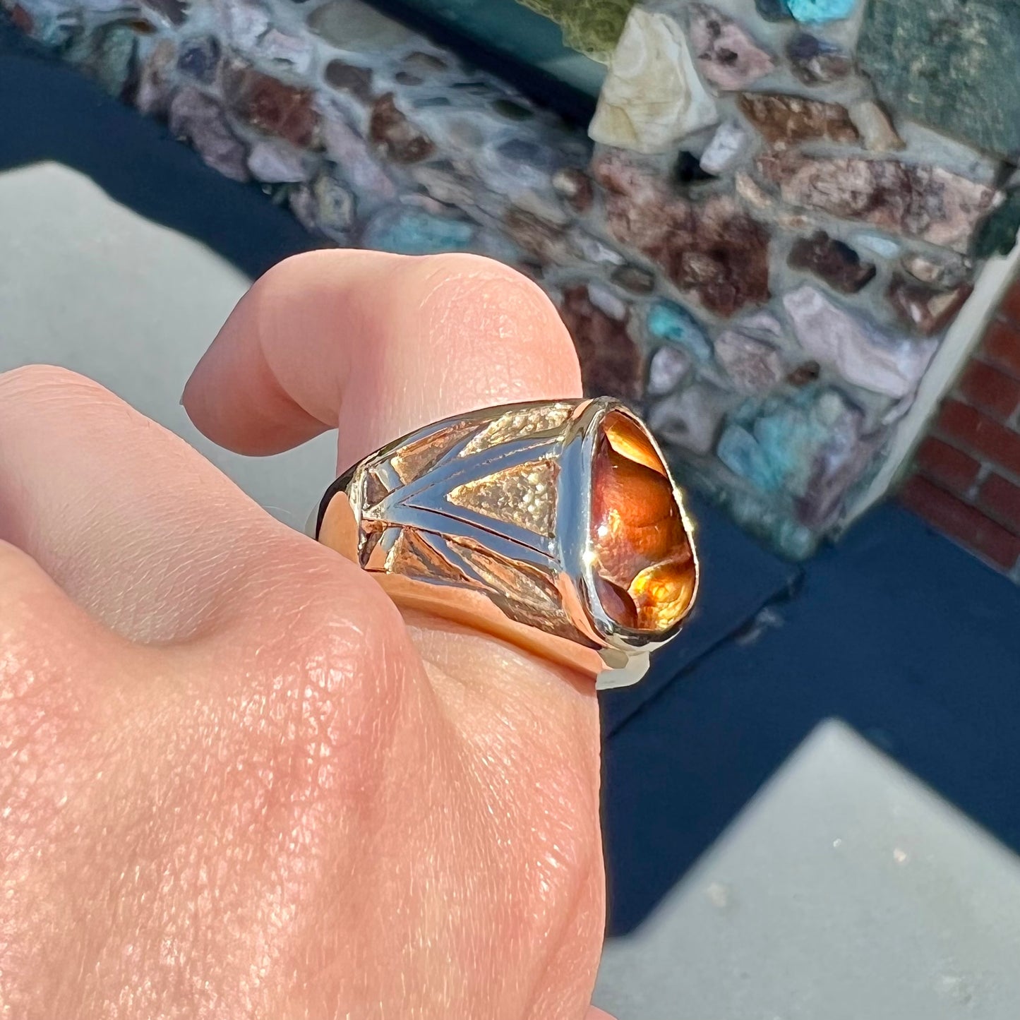 A solid, yellow gold men's fire agate ring. The predominant color is red with green undertones.